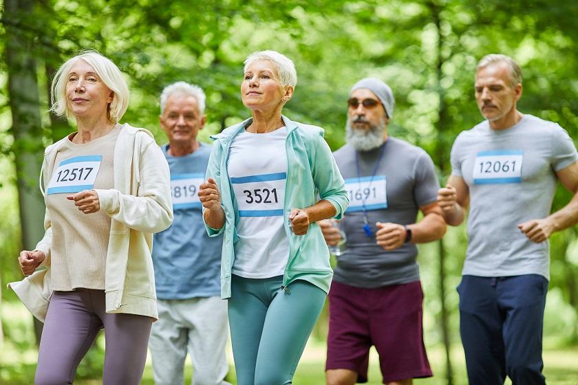 Active senior men and women spending summer day time together in park running marathon, medium long shot